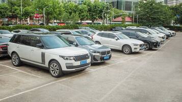 A parking lot with multiple cars, including a white Range Rover and a silver BMW, with buildings and trees in the background.