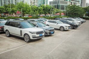 A parking lot with multiple cars, including a white Range Rover and a silver BMW, with buildings and trees in the background.
