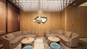Un salon moderne avec deux canapés, des tables rondes et un luminaire au design géométrique suspendu au plafond.