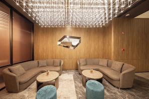 Eine moderne Lounge mit zwei Sofas, runden Tischen und einer geometrischen Leuchtkunstinstallation an der Decke.