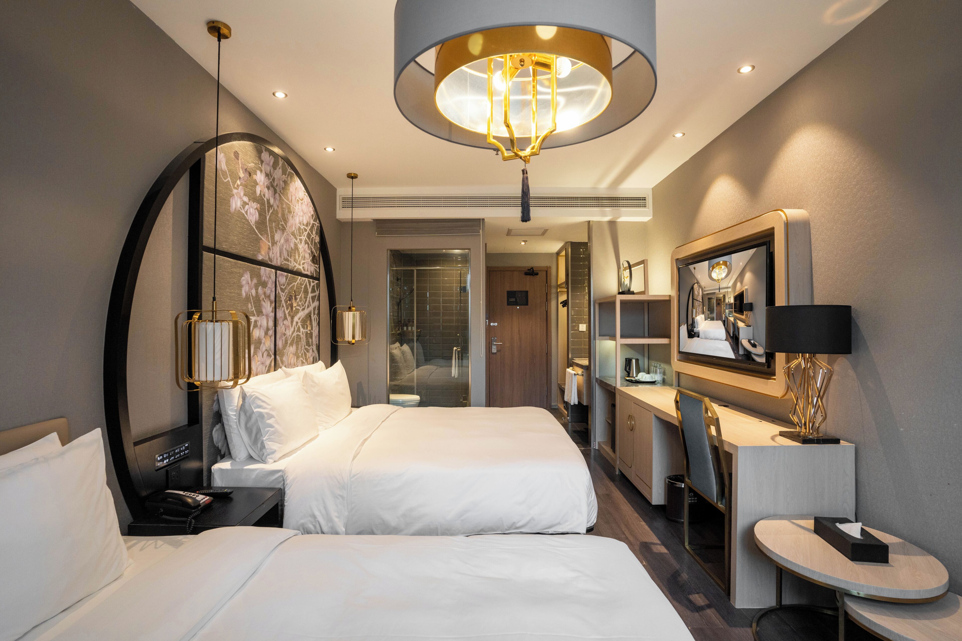 A hotel room with a large bed, a desk, a mirror, and a modern chandelier.