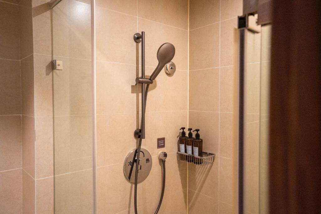 Eine Dusche mit Duschhandstück, einer fest installierten Bedienung und einem Seifenspender.