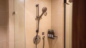 Eine Dusche mit Duschhandstück, einer fest installierten Bedienung und einem Seifenspender.