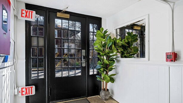 Eine schwarze Tür mit zwei EXIT-Schildern, einem Blumentopf und einem Feuerlöscher an der Wand.