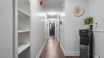 A hallway with white walls, wooden flooring, and a black refrigerator with a water dispenser.