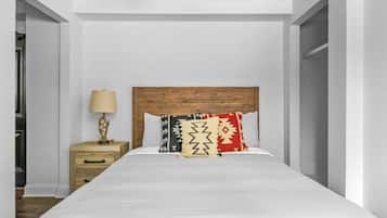 A bedroom with a wooden headboard, a bed with white bedding, a nightstand with a lamp, and a wardrobe.