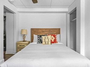 A bedroom with a wooden headboard, a bed with white bedding, a nightstand with a lamp, and a wardrobe. - The Sabel Collection #003 | Downtown Asheville queen suite with Wi-Fi, AC, and parking. (Asheville)