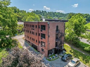 A multi-story brick building with a fire escape, surrounded by greenery and a road. - The Sabel Collection #003 | Downtown Asheville queen suite with Wi-Fi, AC, and parking. (Asheville)