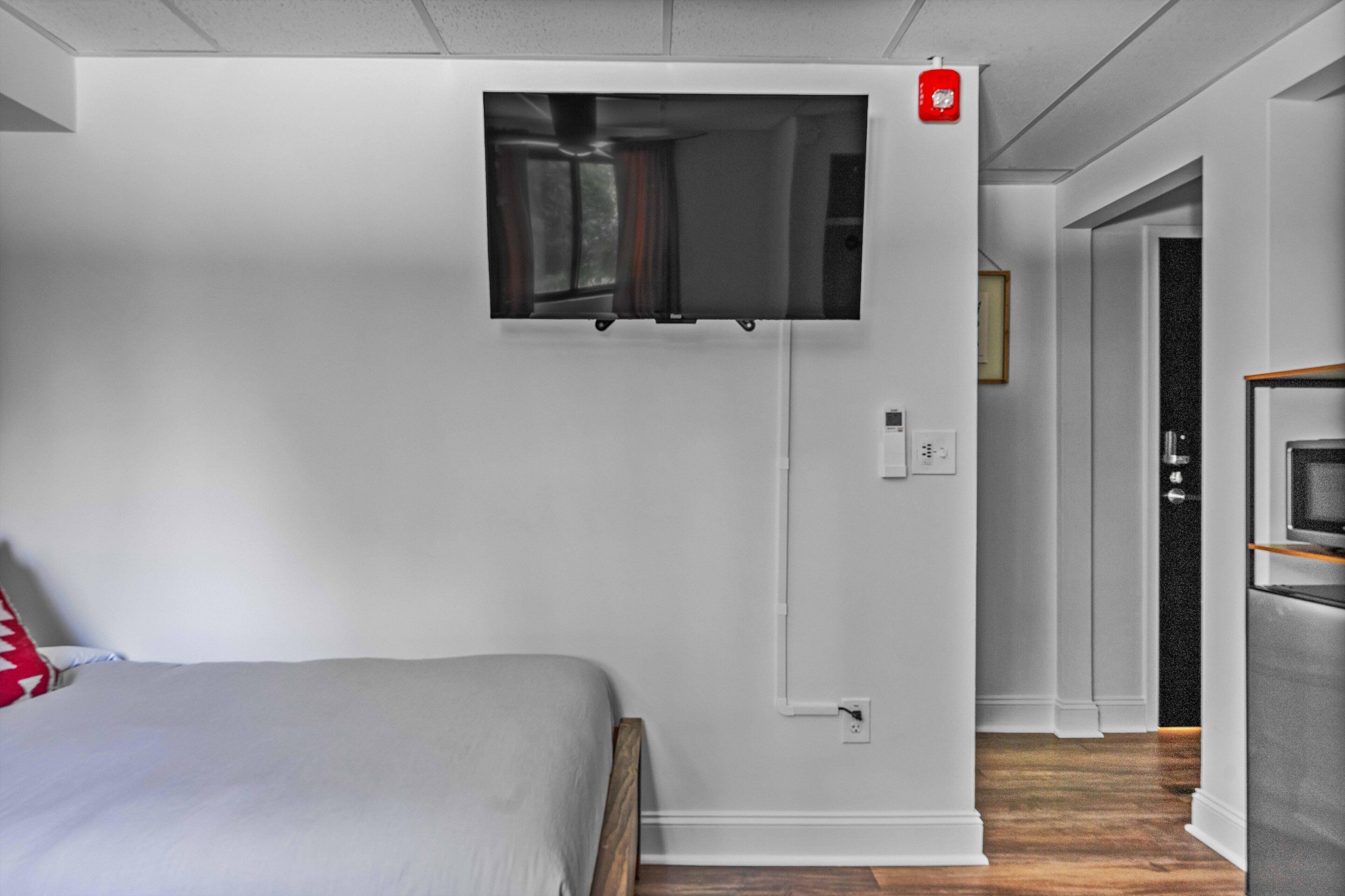 Une chambre d’hôtel moderne équipée d’un lit, d’un téléviseur fixé au mur, d’un coin cuisine avec un four à micro-ondes et d’un couloir menant à une autre chambre.