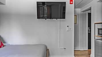Une chambre d’hôtel moderne équipée d’un lit, d’un téléviseur fixé au mur, d’un coin cuisine avec un four à micro-ondes et d’un couloir menant à une autre chambre.