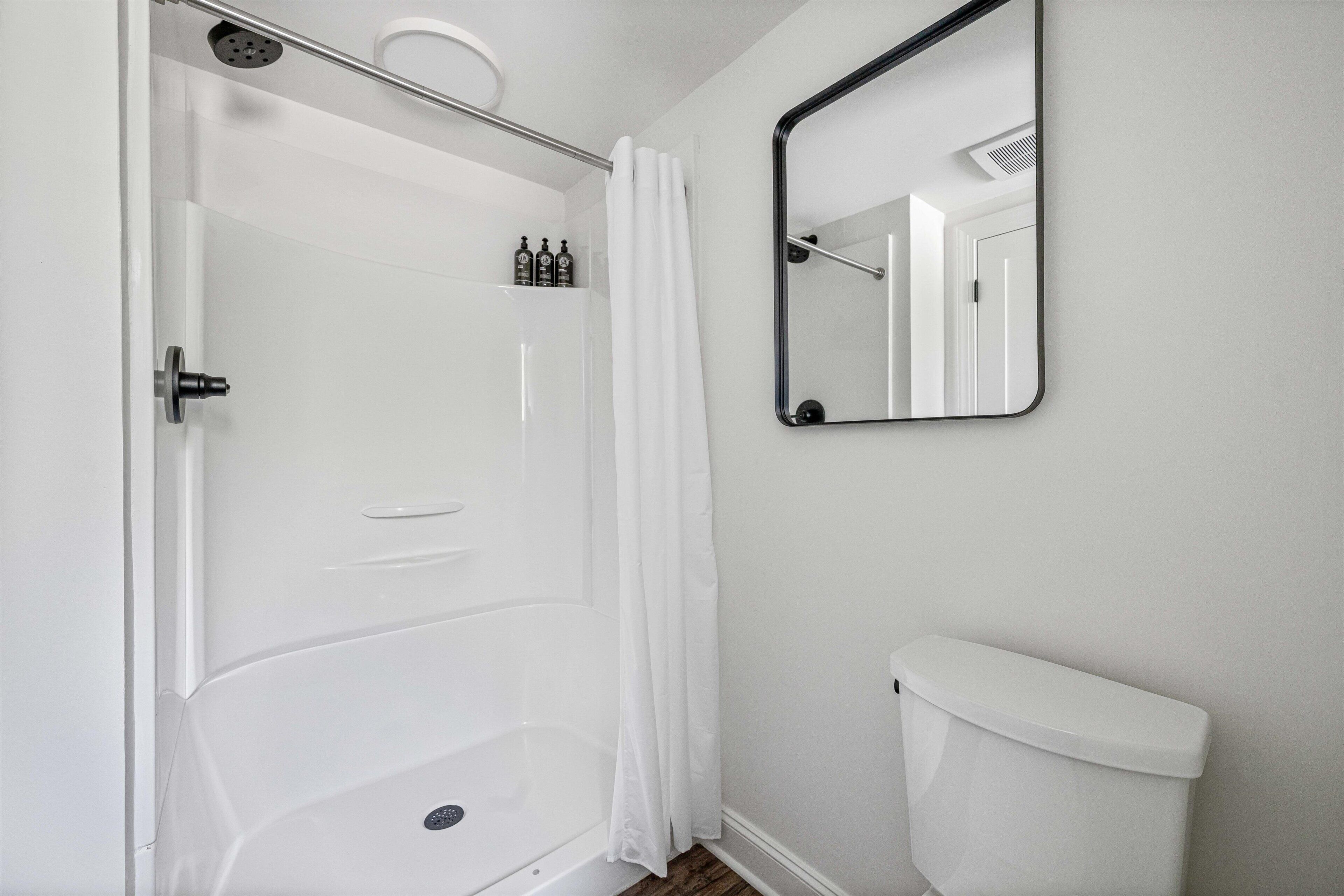 Een badkamer met douche, toilet en spiegel.