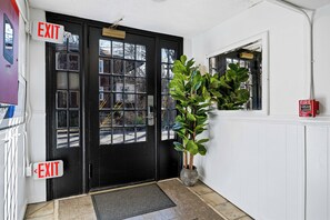 A black door with two EXIT signs, a potted plant, and a fire extinguisher on the wall.