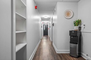 A hallway with white walls, wooden flooring, and a black refrigerator with a water dispenser. - Sabel #004 | Downtown Asheville twin suite with bath, Wi-Fi, AC, and parking. (Asheville)