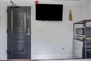Una habitación con puerta negra, televisor de pantalla plana montado, lámpara de pared y estante con microondas integrado.