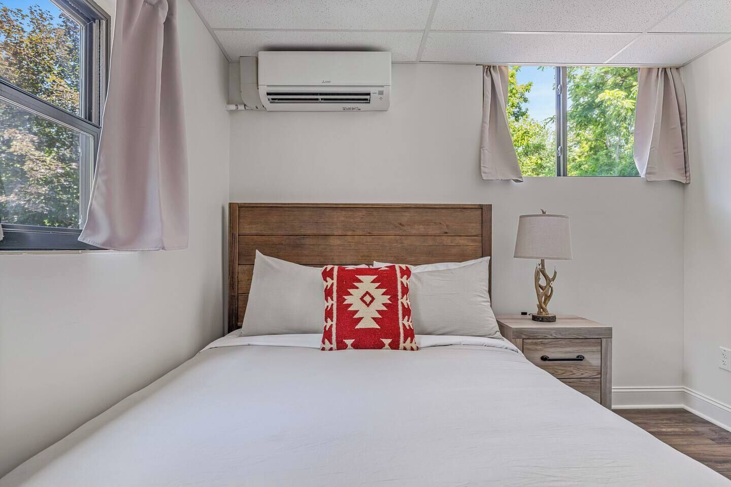 Un lit avec une tête de lit en bois, une lampe de chevet et une fenêtre avec des rideaux.