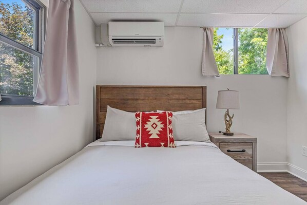 Una cama con cabecera de madera, una lámpara de noche y una ventana con cortinas.