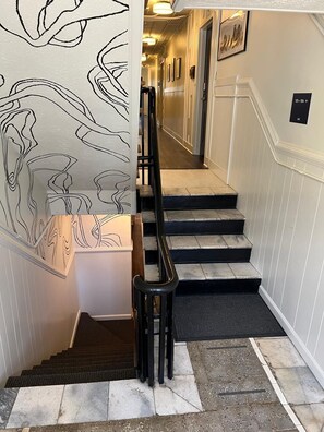 Una escalera con barandilla, peldaños alfombrados y una pared decorada con arte abstracto en líneas.