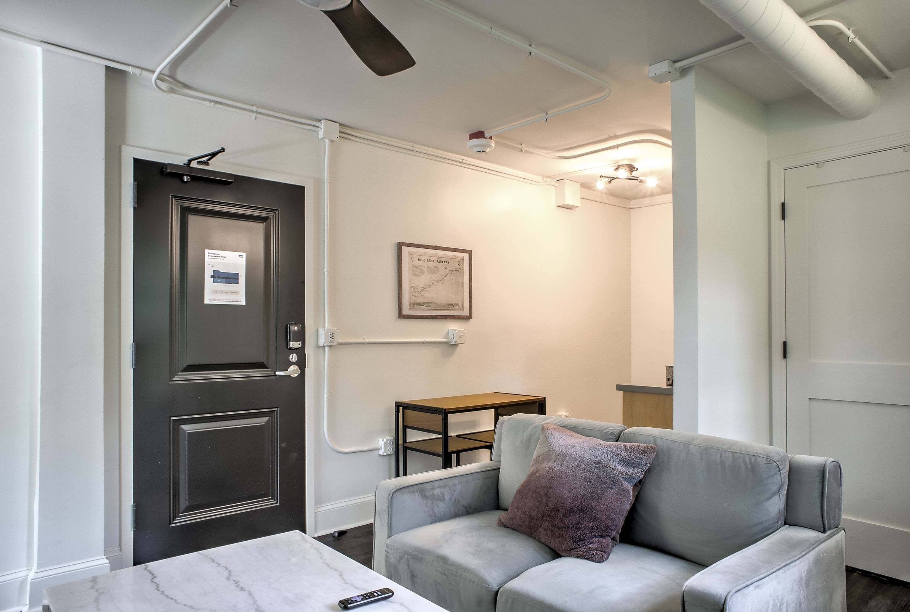 Une pièce avec une porte sombre, un canapé gris avec un coussin, une petite table en bois et une table en marbre.