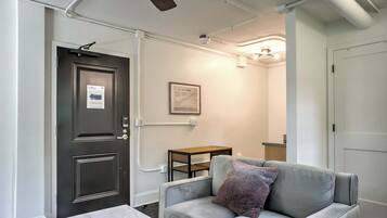 Une pièce avec une porte sombre, un canapé gris avec un coussin, une petite table en bois et une table en marbre.