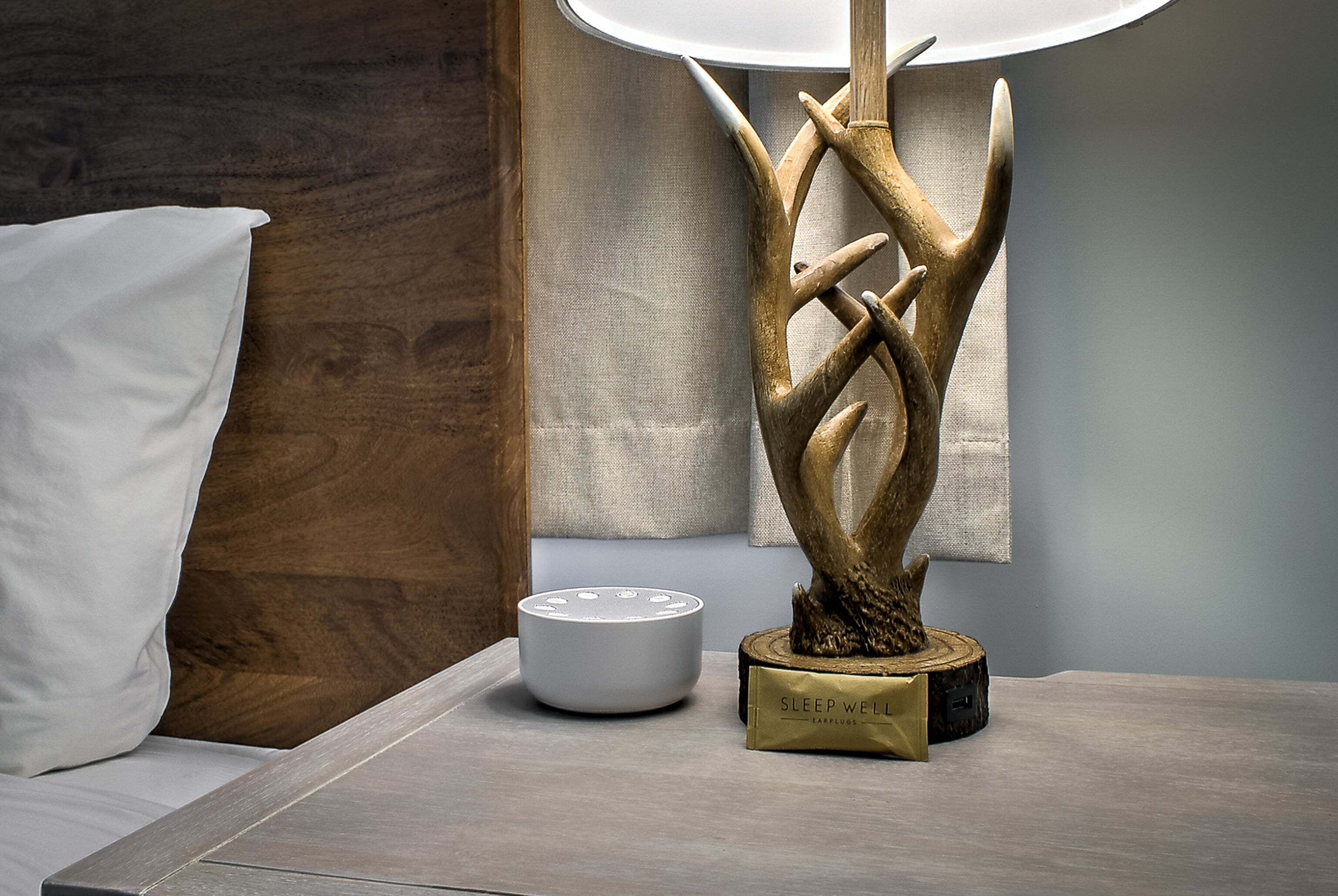 Una camera moderna con una testiera in legno, un cuscino bianco, una scultura decorativa e un comodino con una lampada e un oggetto bianco.