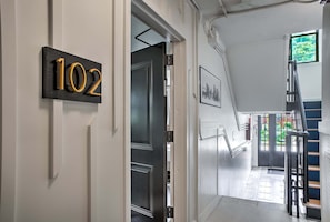 A hallway with a door marked '102', a staircase, and a window with a view of greenery.