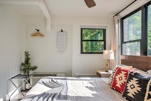 Une chambre à coucher avec un lit, une fenêtre, un radiateur, un porte-manteau mural et une petite plante.