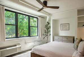 A bedroom with a bed, a radiator, a window with curtains, a ceiling fan, a plant, and a dresser. - Sabel #103 Downtown Asheville king suite with Wi-Fi, parking, and kitchenette (Asheville)