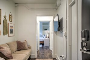 Ein Zimmer mit einem beigen Sofa, einem an der Wand montierten Fernseher und einer Tür zu einem weiteren Raum.
