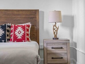 A bed with patterned pillows, a bedside lamp with a tree design, and a wooden nightstand with drawers. - Sabel #103 Downtown Asheville king suite with Wi-Fi, parking, and kitchenette (Asheville)