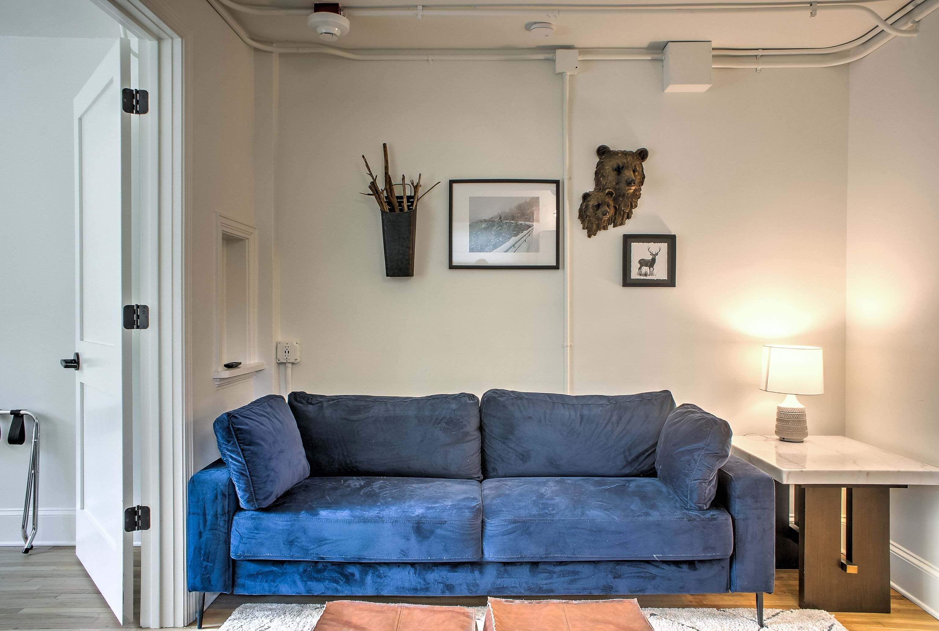 Een kamer met een blauwe bank, een klein tafeltje met een lamp, en wanddecoratie waaronder een foto en een beeld van een beer.