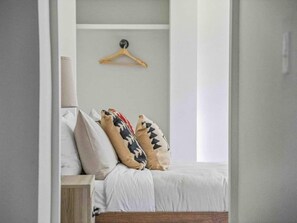 A bedroom with a bed, pillows, a wooden hanger, and a bedside table. - Sabel #202 | King Suite | Downtown Asheville | Fast Wi-Fi & free parking (Asheville)
