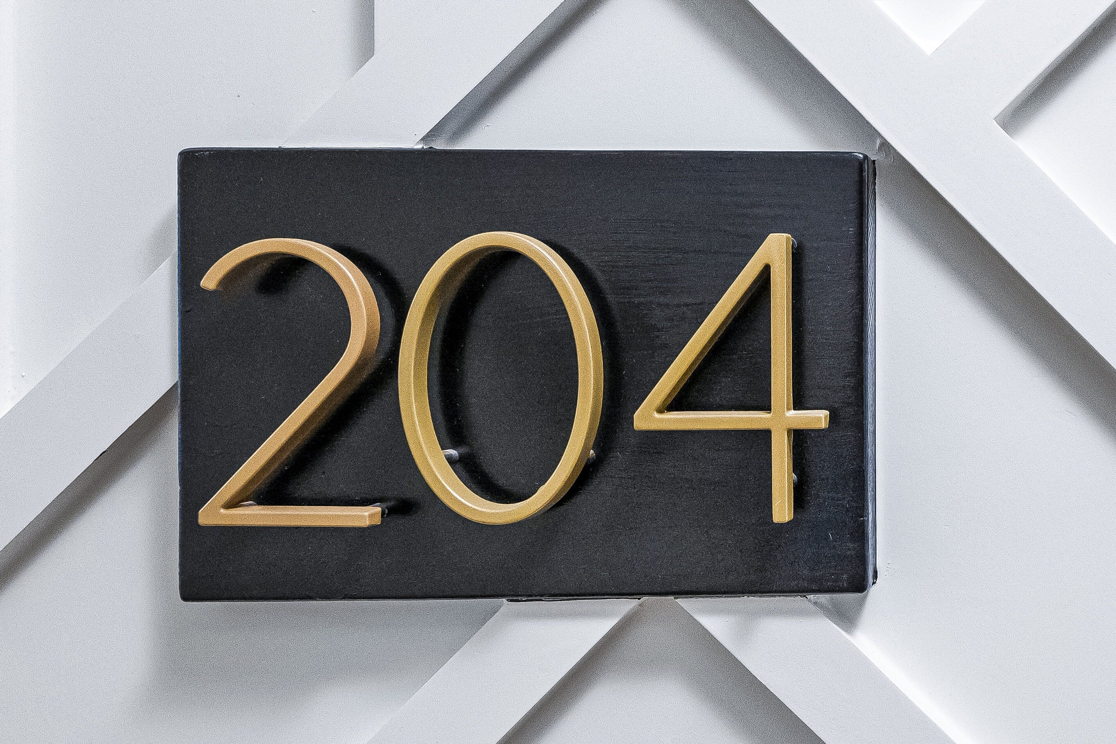 Ein schwarzes Schild mit goldener Beschriftung '204' vor einem weißen Hintergrund mit geometrischem Muster.