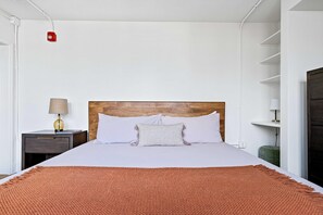 Ein ordentlich eingerichtetes Hotelzimmer mit einem Bett, einem Nachttisch, einer Lampe und einem Regal.