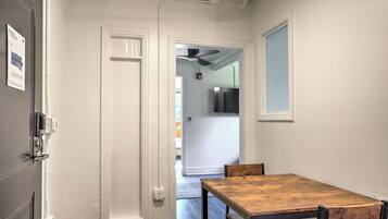 Un couloir étroit avec une table et des chaises en bois, une porte dotée d’une poignée et un ventilateur de plafond.