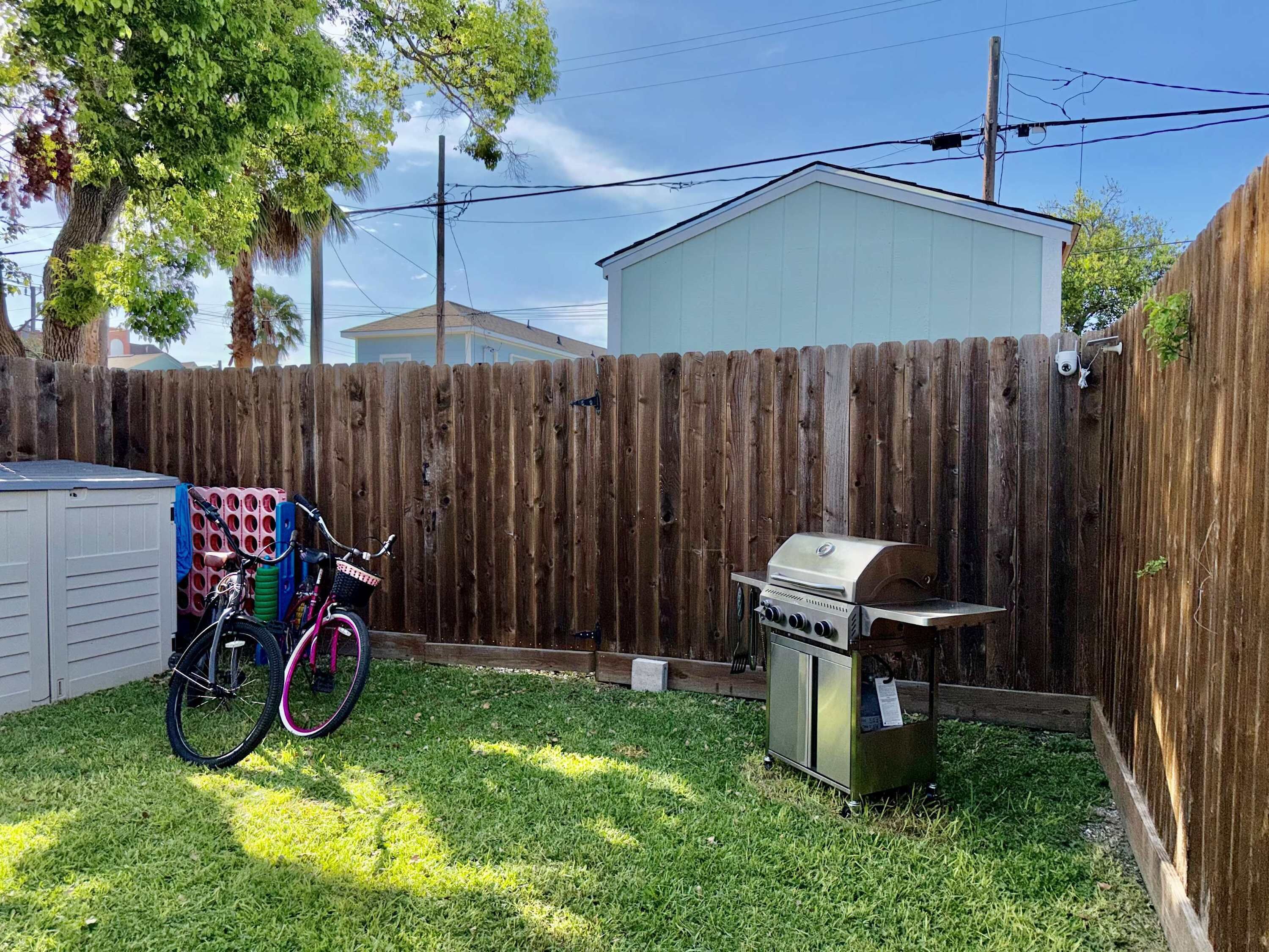 A backyard with a wooden fence, a barbecue grill, and a bicycle with a basket.