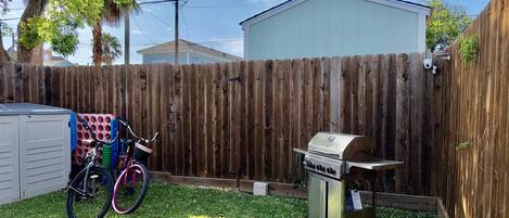 A backyard with a wooden fence, a barbecue grill, and a bicycle with a basket.