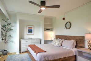Ein Schlafzimmer mit Bett, Nachttisch, Kommode, Deckenventilator, Wandkranz und einer Topfpflanze.