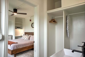 Ein Schlafzimmer mit einem Bett, einem Nachttisch mit Lampe, einem Deckenventilator und einem an der Wand befestigten Regal.