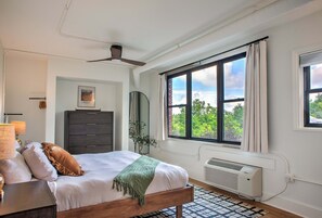 A bedroom with a bed, a dresser, a mirror, a ceiling fan, and a window with a view of trees. - Sabel #304 | Downtown Asheville condo | 1 bed + 1 bath (Asheville)