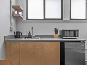 A kitchen with a sink, a kettle, a microwave, and wooden cabinets. - Sabel #304 | Downtown Asheville condo | 1 bed + 1 bath (Asheville)