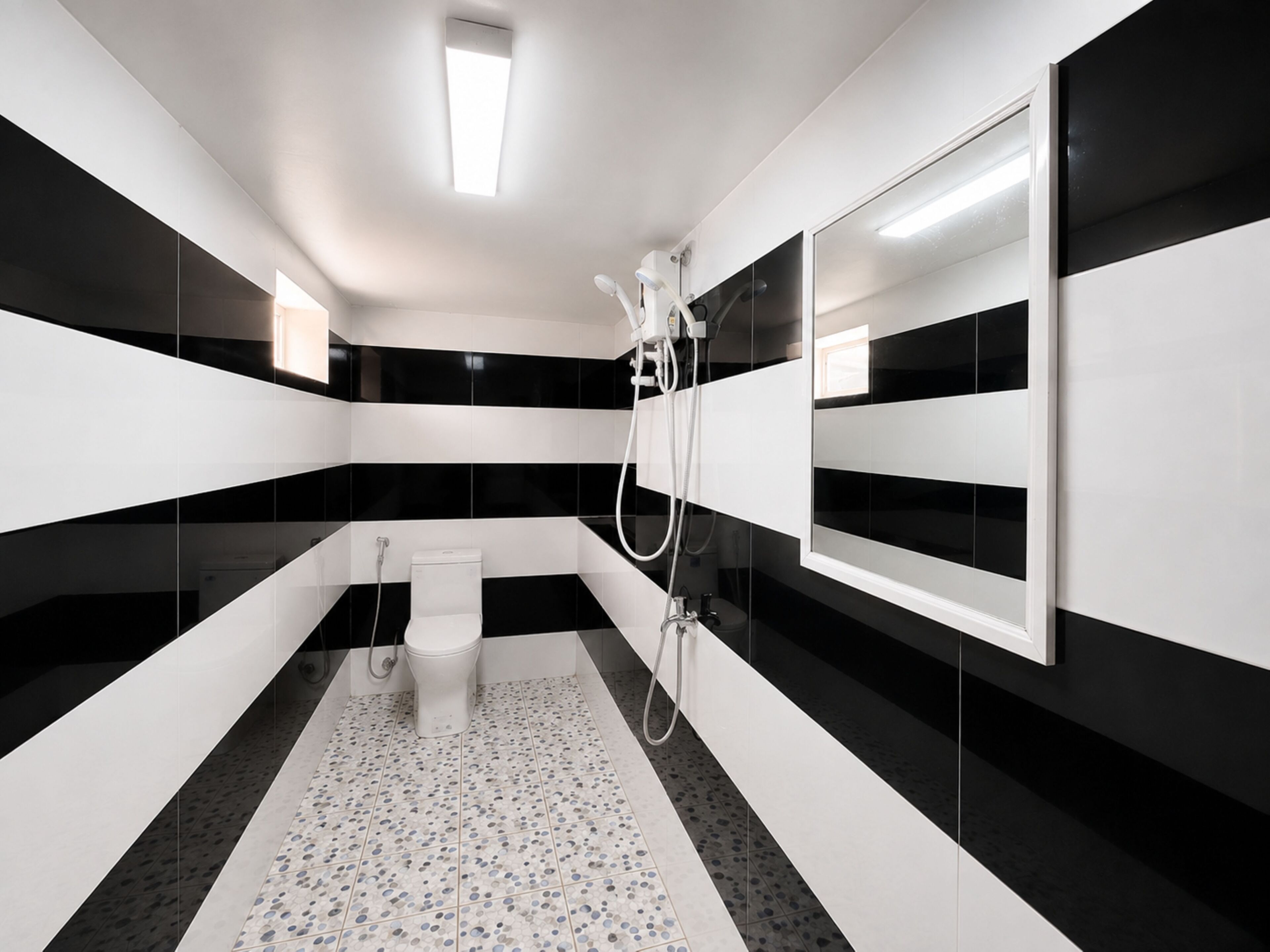 Ein modernes Badezimmer mit schwarzen und weißen Fliesen, einer Toilette, einer Dusche und einem großen Spiegel.
