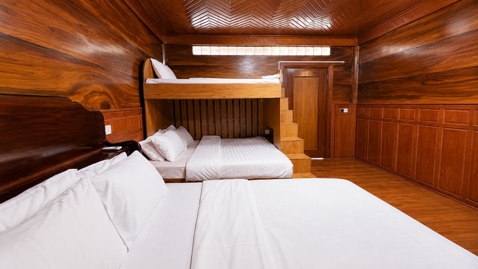 A wooden cabin-style room with bunk beds, a wooden staircase, and a door.