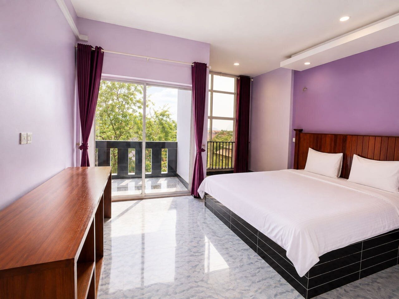 A bedroom with a bed, a wooden desk, and a balcony with curtains.