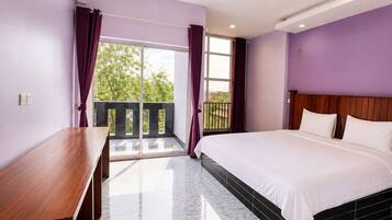 A bedroom with a bed, a wooden desk, and a balcony with curtains.