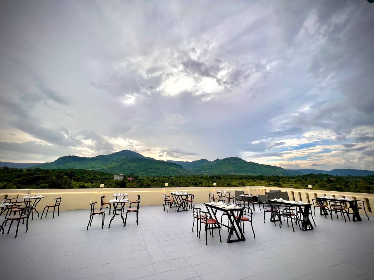 An outdoor dining area with tables and chairs, overlooking a mountainous landscape.