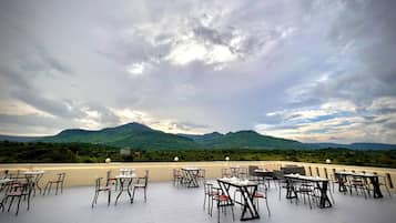 An outdoor dining area with tables and chairs, overlooking a mountainous landscape.