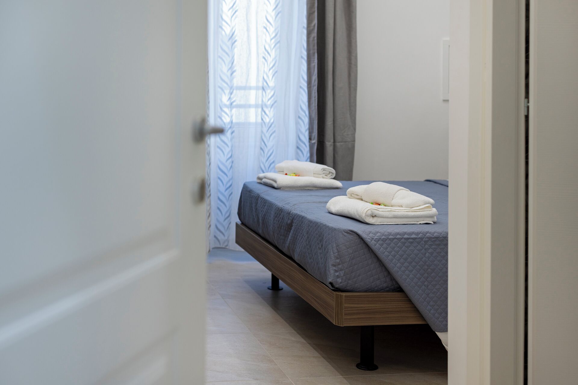 A bedroom with a bed, a door, and a window with curtains.