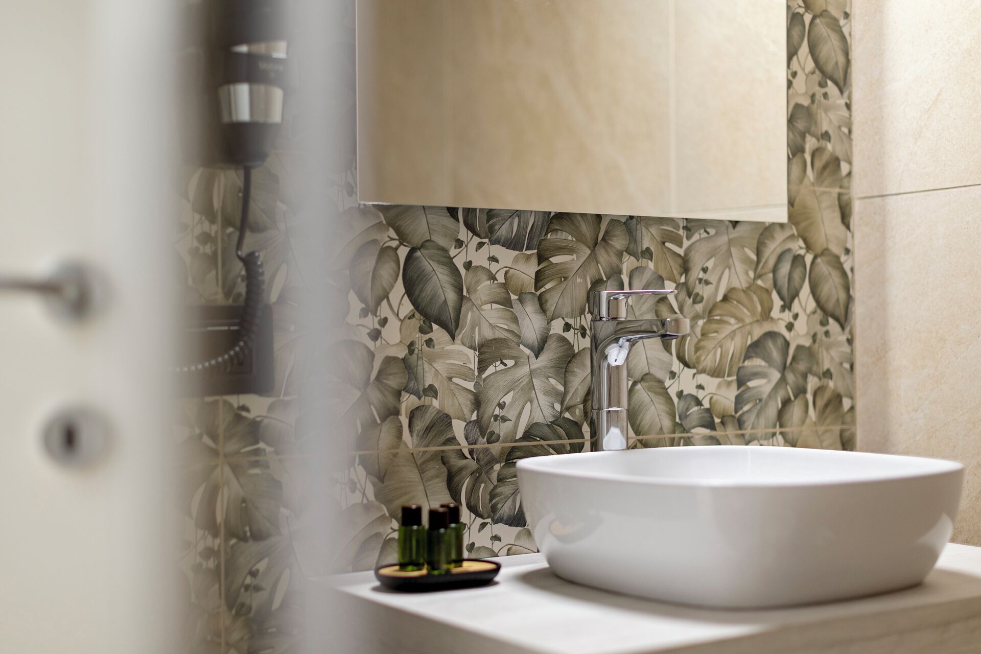 Une salle de bain avec un lavabo blanc, un robinet moderne et un mur décoratif orné de motifs de feuilles.