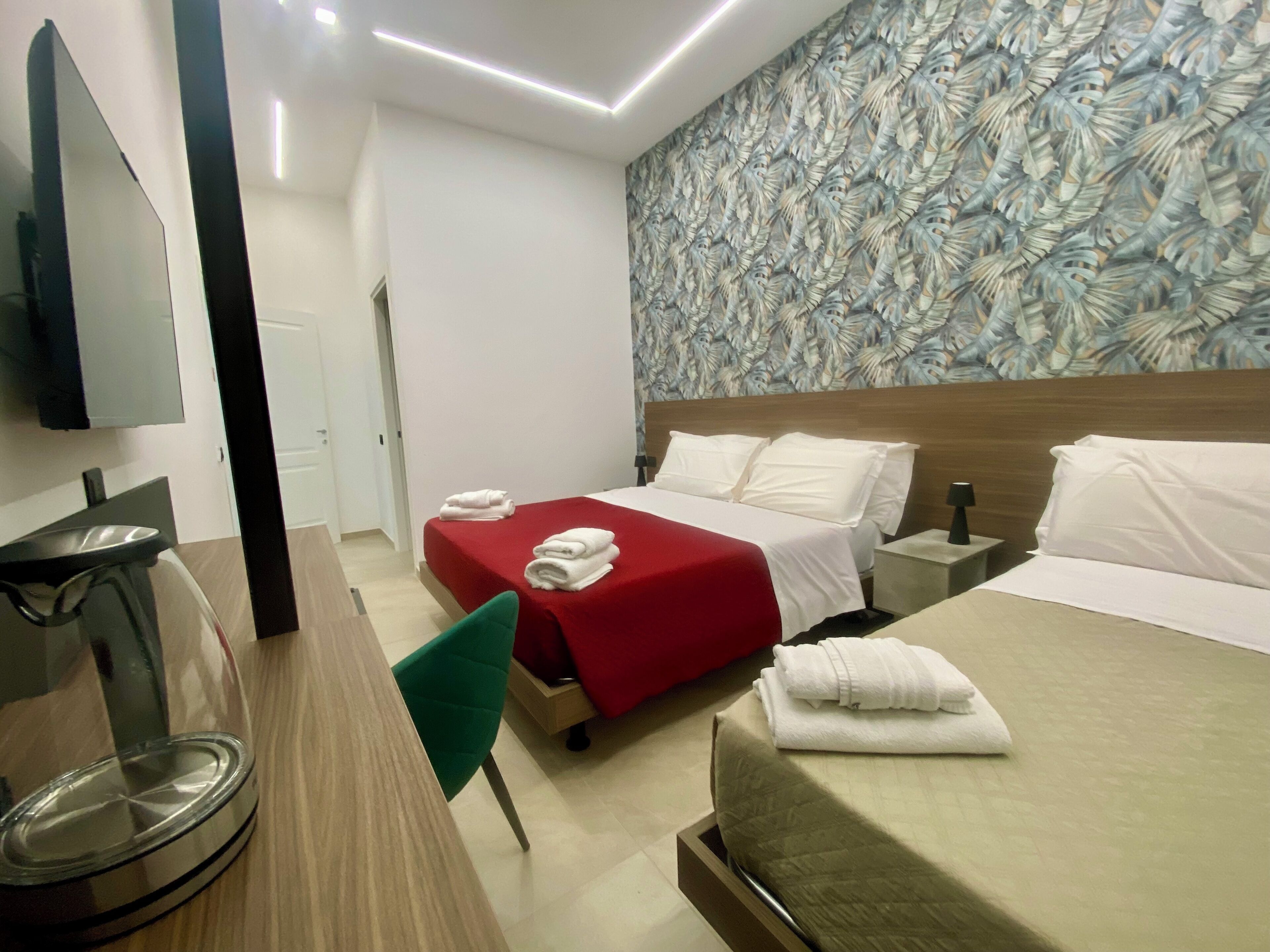 A hotel room with two beds, a desk, a chair, a TV, and a patterned wall.