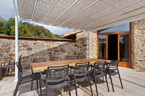 Un pati exterior amb mur de pedra, taula de fusta i cadires negres.